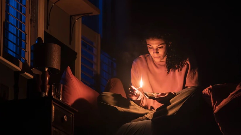 Stage scene from a paranormal activity play featuring actors in suspenseful poses with dim lighting and eerie props.