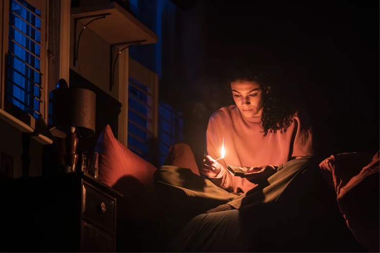 Stage scene from a paranormal activity play featuring actors in suspenseful poses with dim lighting and eerie props.