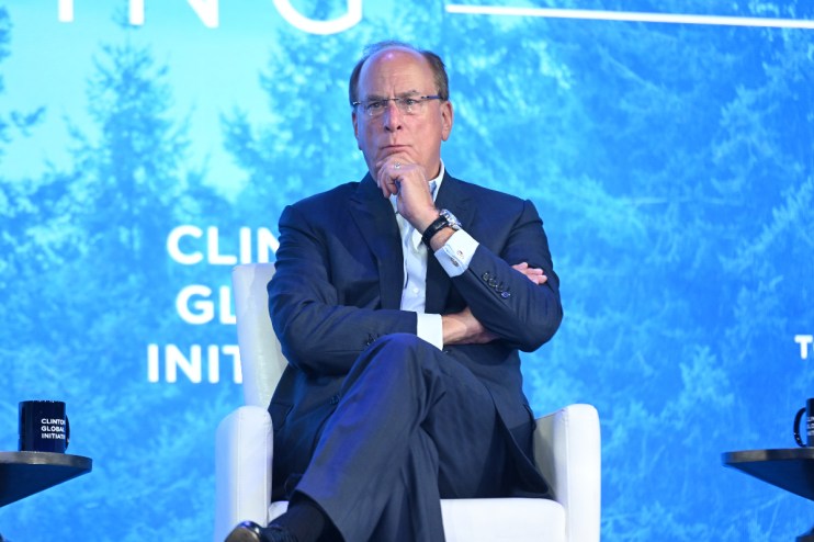 Larry Fink, CEO of BlackRock, speaking at a business conference, wearing a suit and glasses, gesturing with his hands