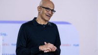 Satya Nadella, CEO of Microsoft, speaking at a tech conference, wearing a suit, with a backdrop of the Microsoft logo