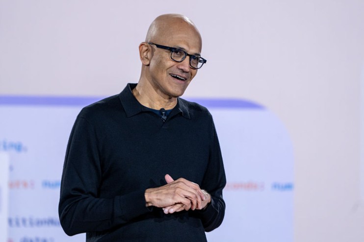 Satya Nadella, CEO of Microsoft, speaking at a tech conference, wearing a suit, with a backdrop of the Microsoft logo