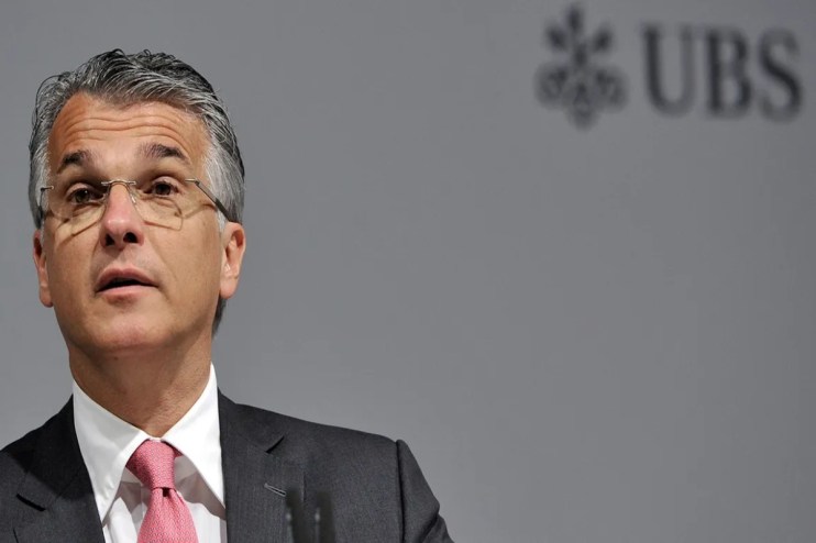 Sergio Ermotti, UBS CEO, addressing media at a press conference, wearing a suit and glasses, with a serious expression