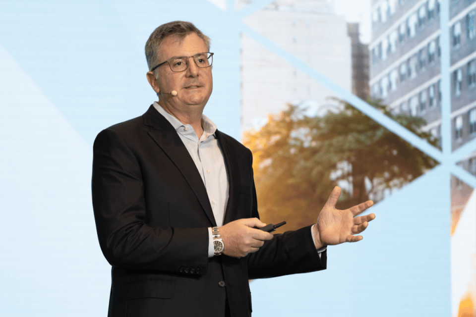 Erick Hirsch, CEO of Hamilton Lane, in a business suit, confidently addresses a conference audience at a corporate event.