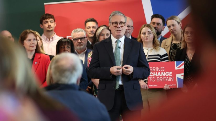 Labour Party leaders discussing policy strategies at a conference, with banners and attendees in the background