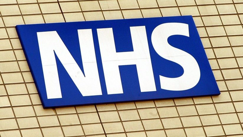 NHS healthcare professionals in a hospital setting discussing patient care plans, wearing uniforms and medical equipment v...