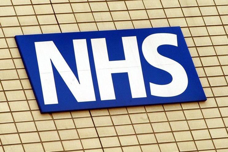 NHS healthcare professionals in a hospital setting discussing patient care plans, wearing uniforms and medical equipment v...
