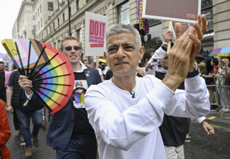 Sadiq Khan proudly participating in a vibrant Pride parade, surrounded by colorful flags and joyful attendees in London.