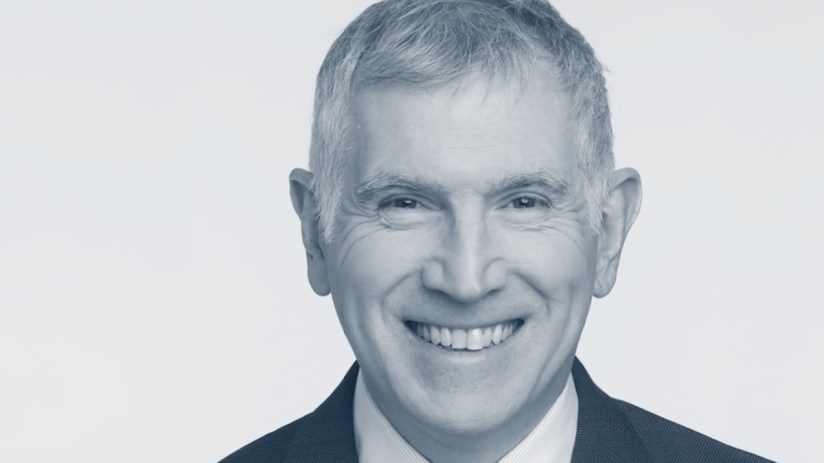 Tim Allan discussing business trends at a corporate event, wearing a suit and speaking on stage with a presentation screen.