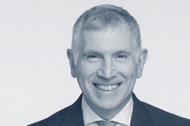 Tim Allan discussing business trends at a corporate event, wearing a suit and speaking on stage with a presentation screen.