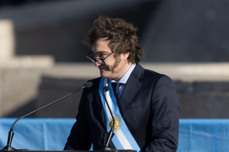 JavierMalei presents a keynote speech at a business conference, engaging with a diverse audience in a modern auditorium.