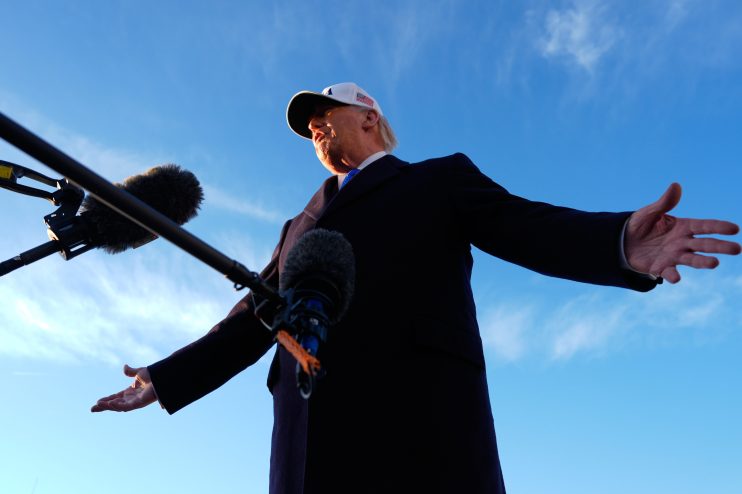 President Trump delivering a speech at a podium, emphasizing national policies, with American flags in the background.