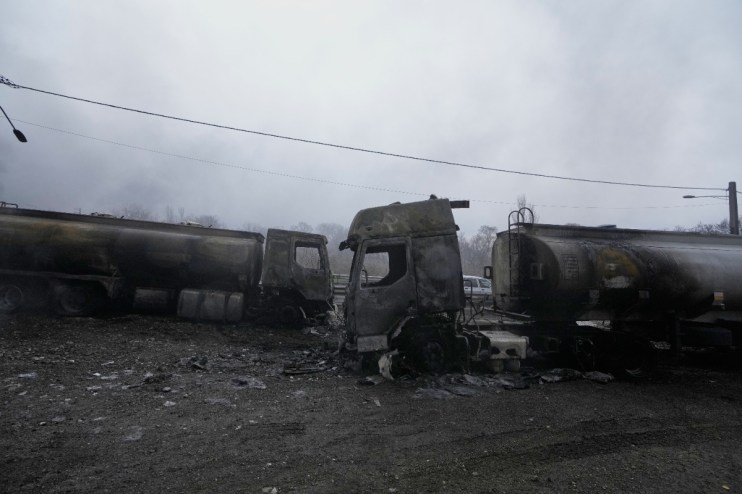 Charred oil tankers aftermath of an explosion at a refinery, with smoke billowing and emergency crews assessing the damage.