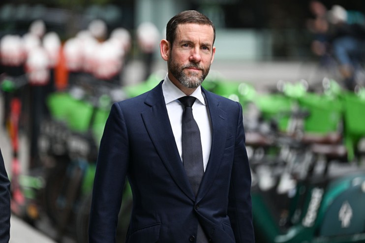 Lex Greensill speaking at a business conference, wearing a suit and tie, gesturing with his hand while discussing financia...