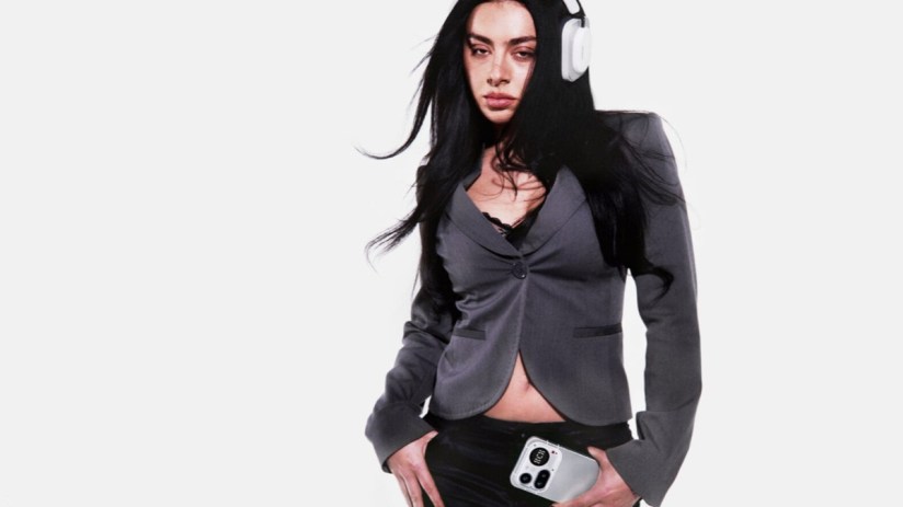 Charli XCX wearing stylish headphones at an event promoting her latest music project, showcasing her unique fashion sense.