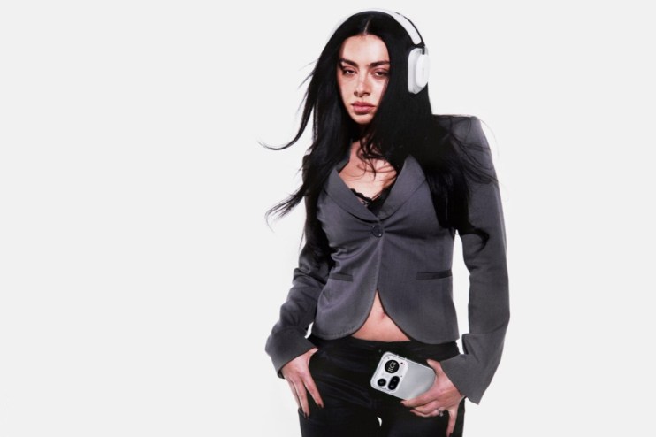 Charli XCX wearing stylish headphones at an event promoting her latest music project, showcasing her unique fashion sense.