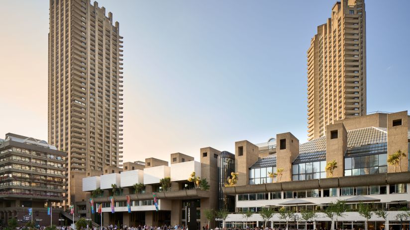 Dion Barrett captures a bustling city street scene with diverse pedestrians and vibrant storefronts on a sunny day.
