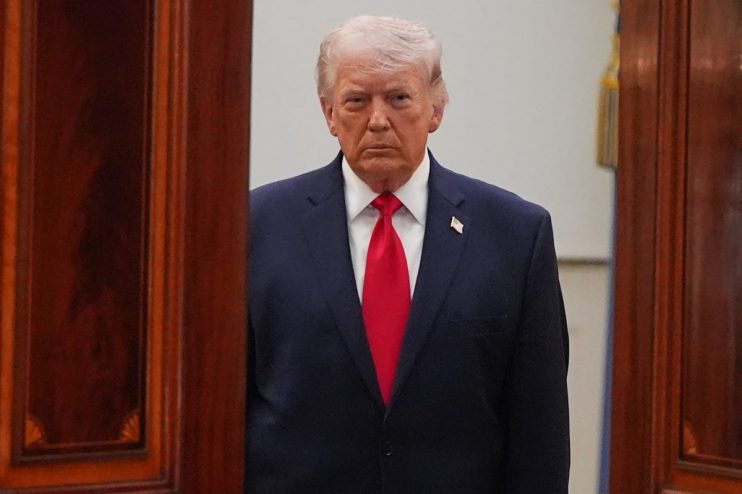 Donald Trump speaking at April event, wearing a suit and tie, with an expressive gesture and a serious facial expression