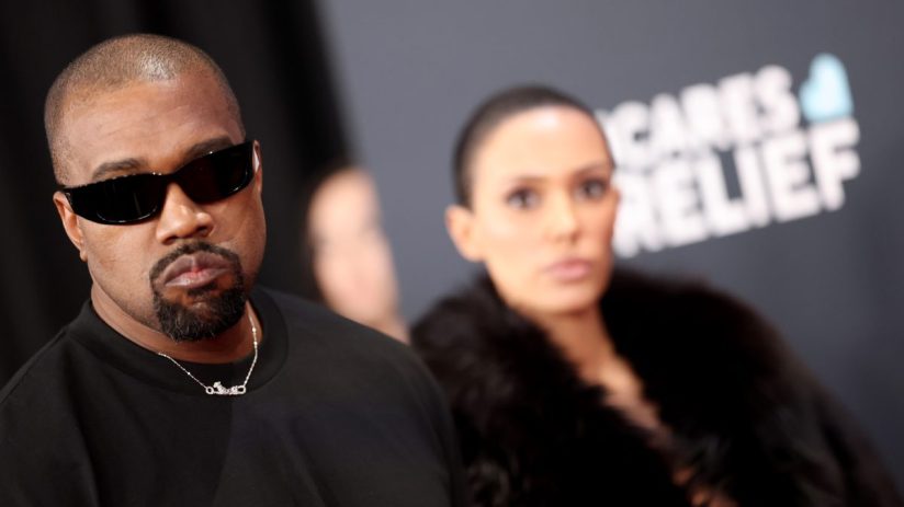 Kanye West attending a public event, wearing stylish attire, capturing media attention amidst ongoing news discussions