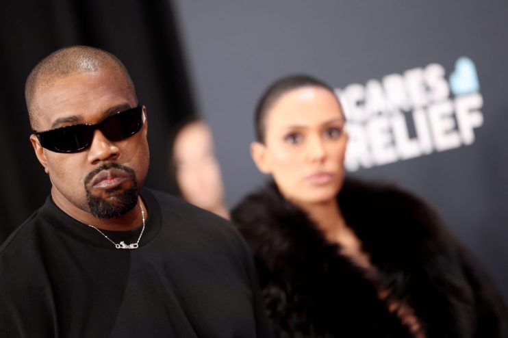 Kanye West attending a public event, wearing stylish attire, capturing media attention amidst ongoing news discussions