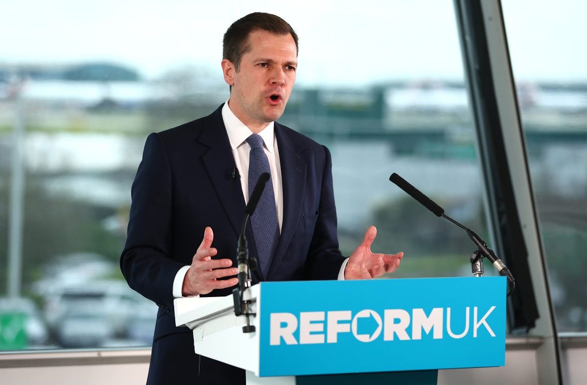 Robert Jenrick speaking at a press conference, addressing current policy issues, wearing a suit and standing behind a podium