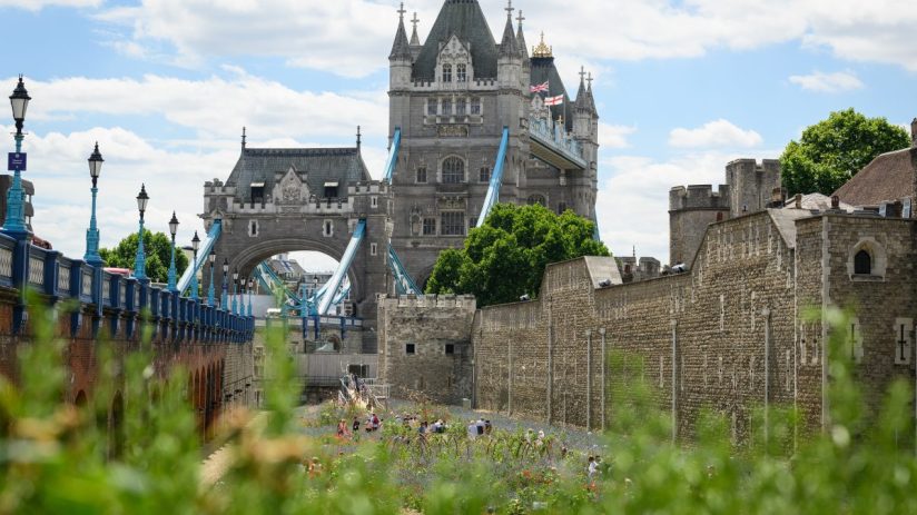 Historic Tower of London under clear blue sky, showcasing iconic medieval architecture and stone walls, attracting tourist...