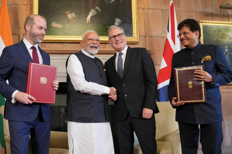 UK and India representatives signing trade agreement at formal meeting with flags and documents visible on the table