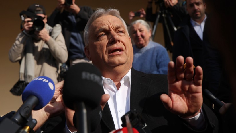 Hungarian Prime Minister Viktor Orban speaking at a press conference, gesturing with his hands, with a serious expression.