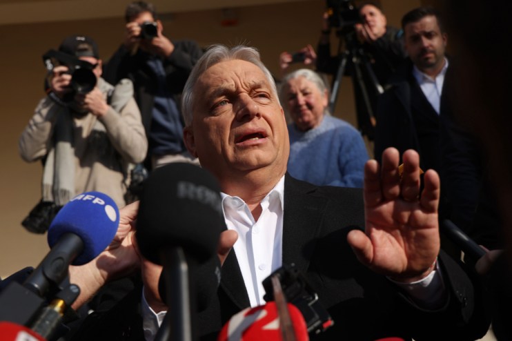 Hungarian Prime Minister Viktor Orban speaking at a press conference, gesturing with his hands, with a serious expression.