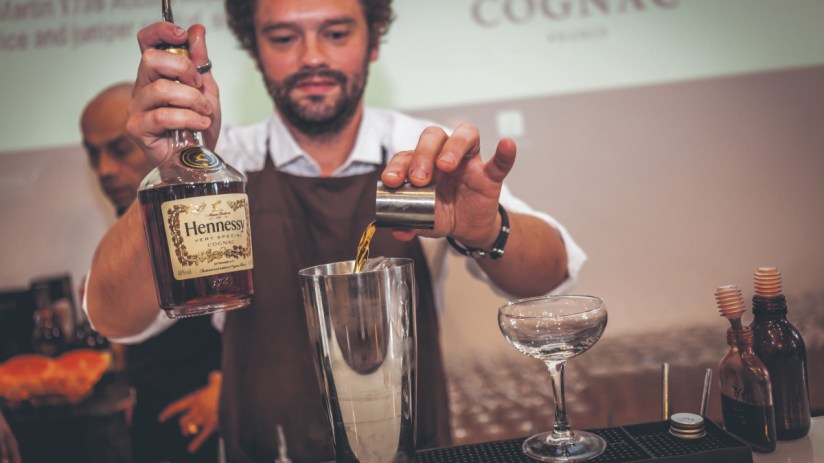 Hennessy expert crafting vibrant cocktails at the Cognac Show utilizing CYMK color techniques for mixology art