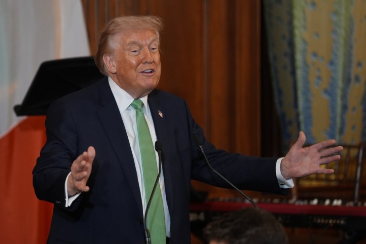 Donald Trump wearing a green tie at a public event, addressing the audience with a serious expression in a formal setting