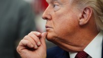 Donald Trump with hand on chin, appearing contemplative during a public event, wearing a suit and red tie.