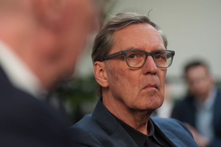 Alan Milburn delivering a speech at a press conference, wearing a suit and tie, addressing economic policy issues.