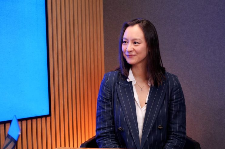 Alisha smiling confidently in professional attire, standing in a modern office environment reflecting business success.