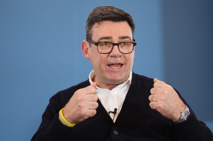 Andy Burnham speaking at a public event, wearing a suit, addressing an audience with a focused expression and engaged deme...
