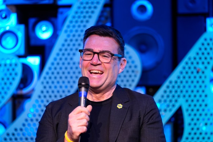 Andy Burnham speaking at a public event, addressing key issues in Manchester, wearing a suit and gesturing with his hands