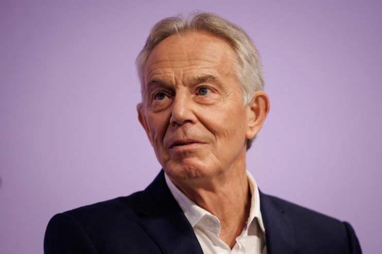 Tony Blair delivering a speech at a conference podium, discussing current global political issues.