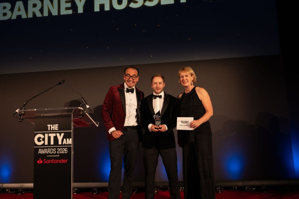 Barney receiving award at Morning Wire Awards ceremony, surrounded by applauding attendees in formal attire