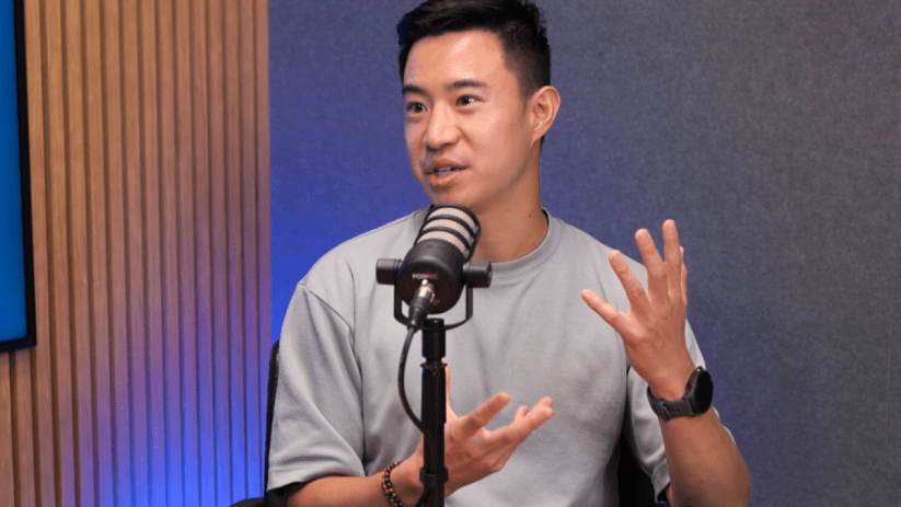 Corvera Christopher Kong at a business event, wearing a suit and speaking at a podium with a branded backdrop.