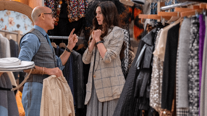 Anne Hathaway in a cut scene from Devil Wears Prada 2, wearing a stylish outfit, surrounded by high fashion elements.