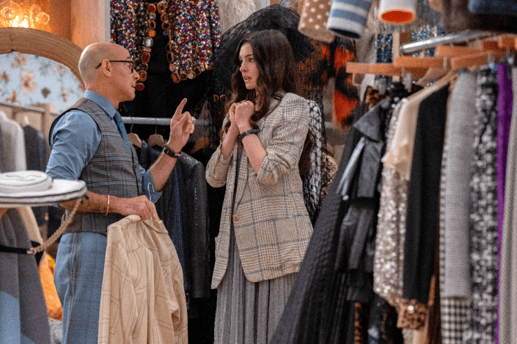 Anne Hathaway in a cut scene from Devil Wears Prada 2, wearing a stylish outfit, surrounded by high fashion elements.