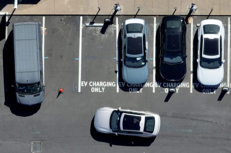 Electric vehicle charging station with multiple charging ports and cars plugged in, promoting sustainable transportation s...