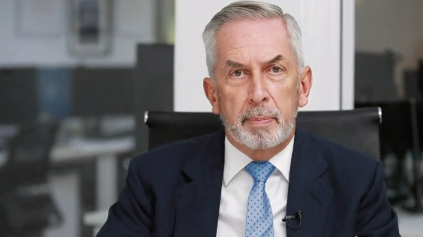 Terry Smith, founder of Fundsmith, speaking at a business conference, wearing a suit and tie, with a focused expression.