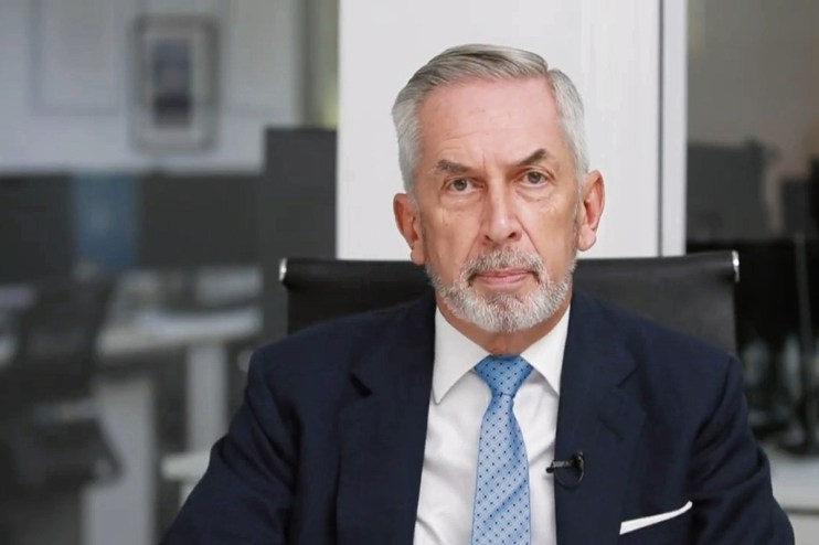 Terry Smith, founder of Fundsmith, speaking at a business conference, wearing a suit and tie, with a focused expression.