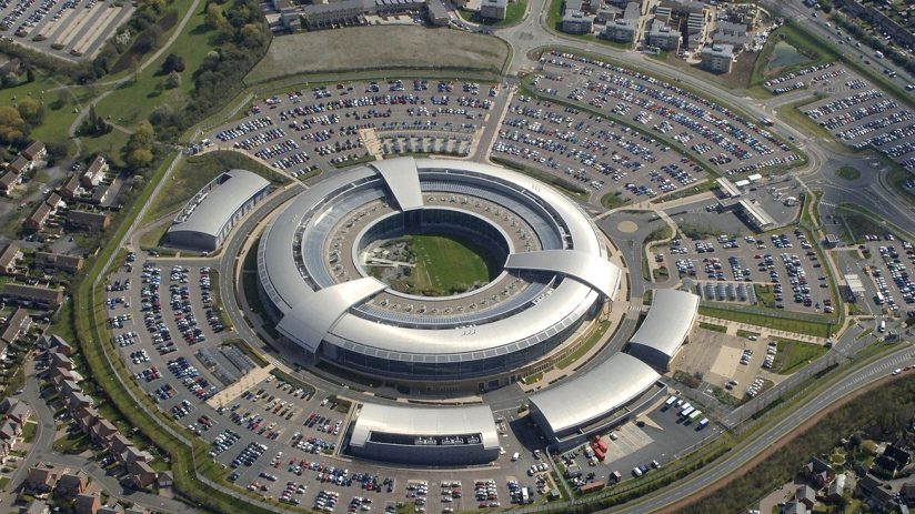 GCHQ headquarters at dusk with illuminated windows, showcasing the iconic circular building amidst a vibrant evening sky.