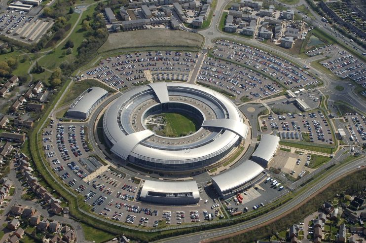 GCHQ headquarters at dusk with illuminated windows, showcasing the iconic circular building amidst a vibrant evening sky.