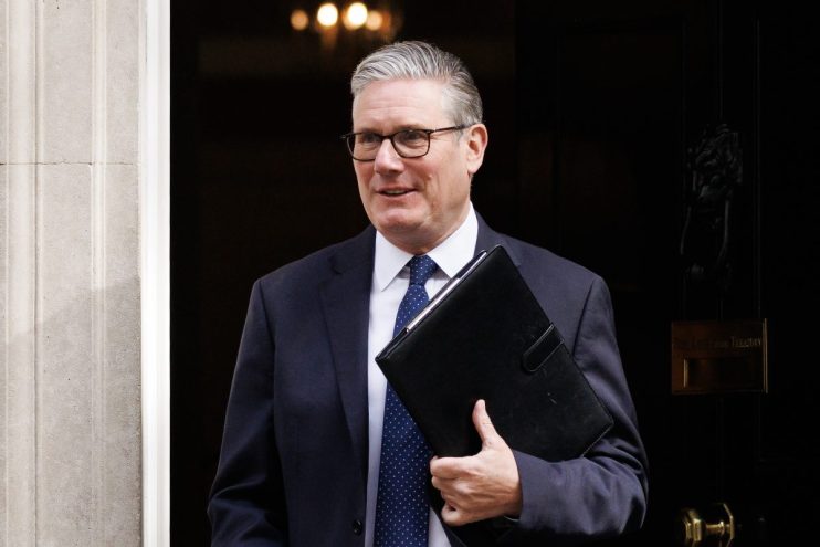 Keir Starmer speaking at a podium, addressing an audience in a formal setting, wearing a suit and tie, in a news conference
