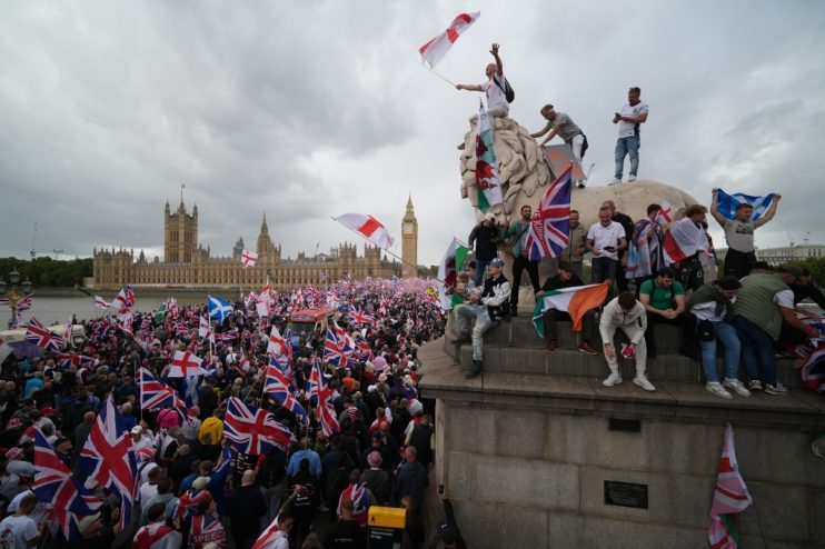 Crowd gathers in London for Unite the Kingdom rally, holding banners and flags, advocating for national unity and solidarity.