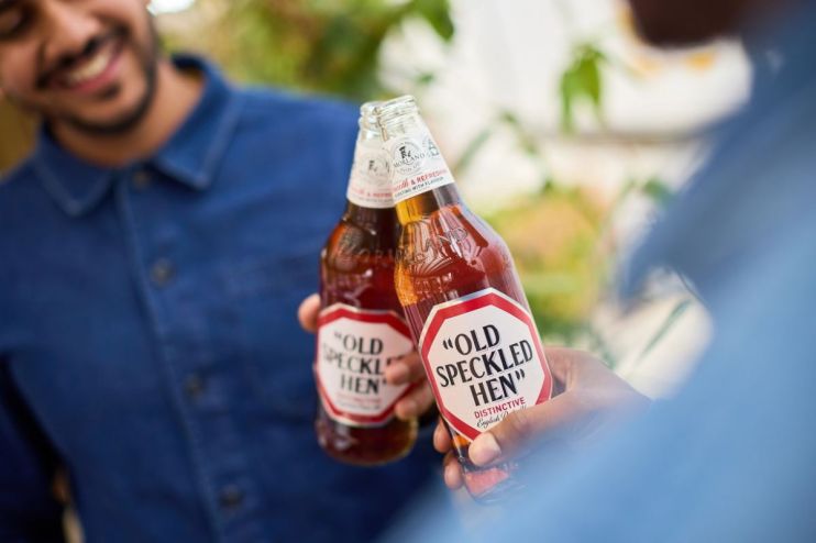 Old Speckled Hen beer bottle with label visible on a wooden table, showcasing its classic design and distinctive branding