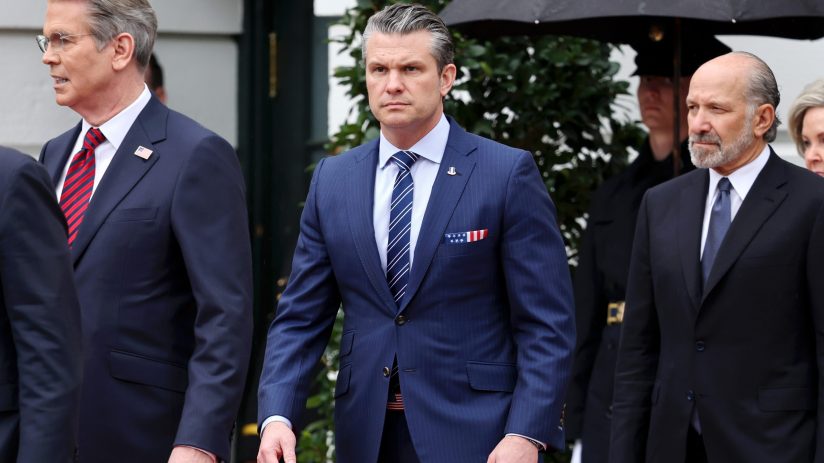 Pete Hegseth speaking passionately at a news conference podium with a focused audience in the background