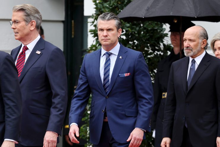 Pete Hegseth speaking passionately at a news conference podium with a focused audience in the background